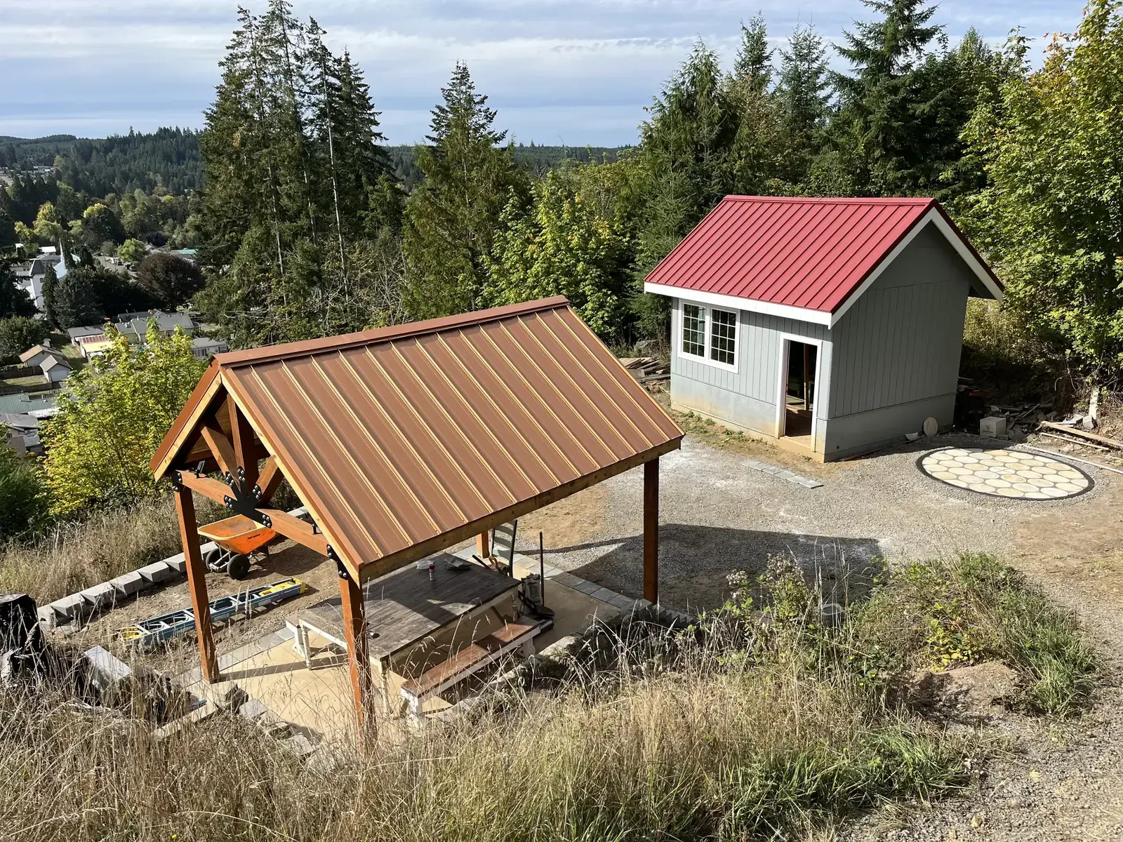 A round paver fire-pit pad between a covered pavilion and a tiny house